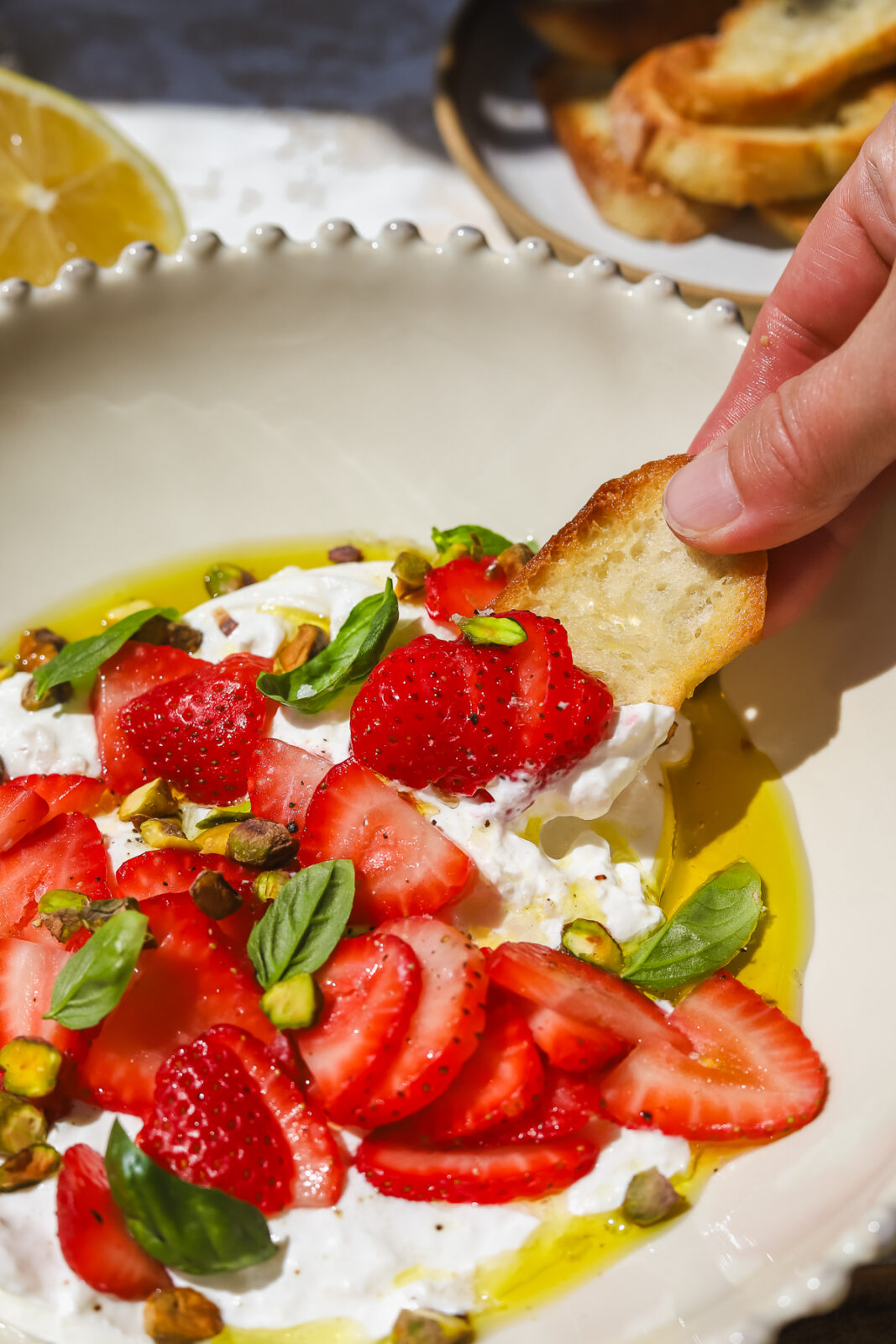 hand dipping crostini into strawberry burrata appetizer in a bowl