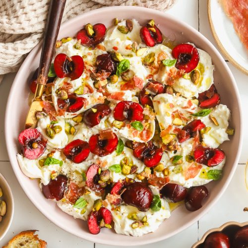 plate of burrata and prosciutto with fresh cherries and basil