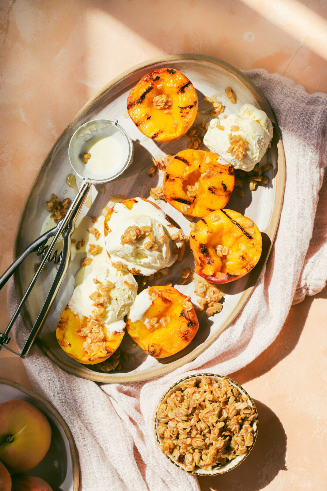 grilled peaches on a serving tray with scoops of ice cream and oat crumble
