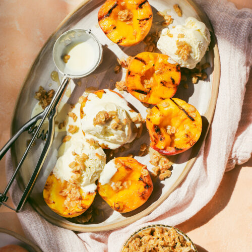 grilled peaches on a serving tray with scoops of ice cream and oat crumble