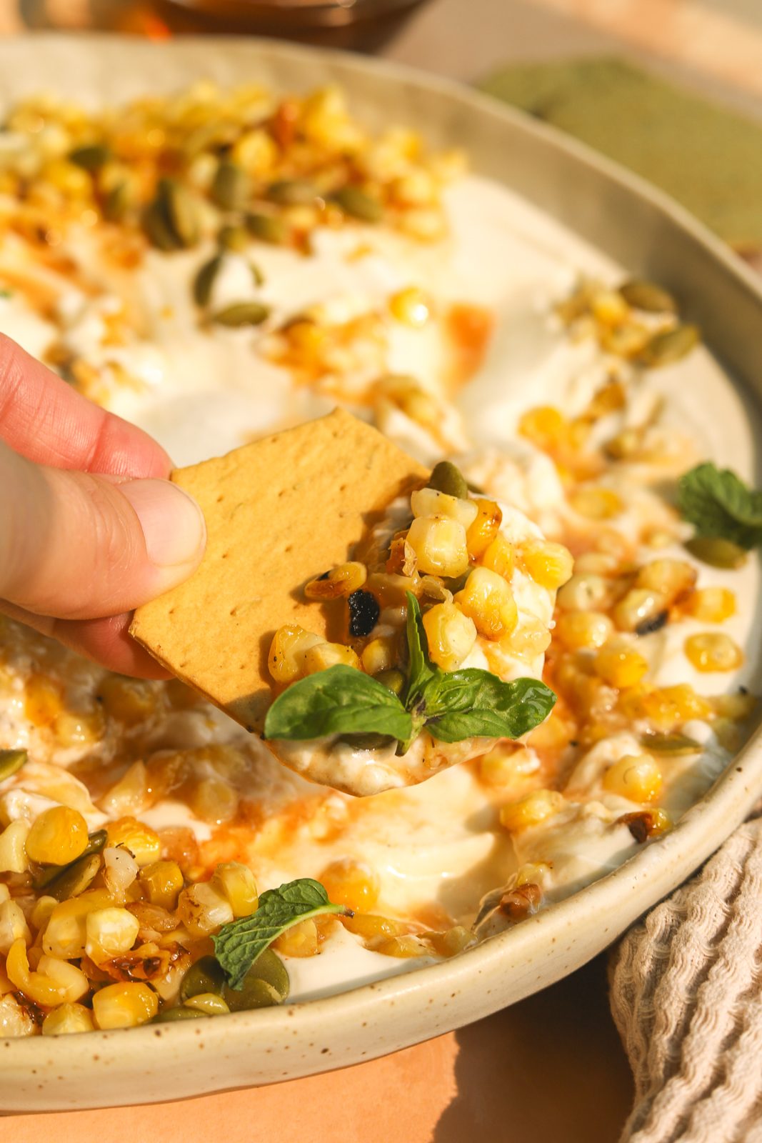 cracker scooping whipped feta with hot honey and charred corn