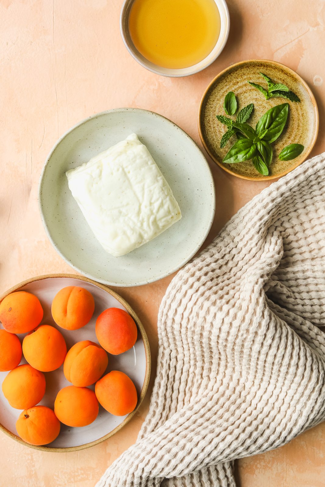 whole piece of halloumi on a plate, apricots on a plate, fresh mint on a plate, honey in a bowl