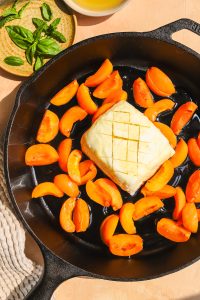 piece of halloumi cheese with honey drizzle on it in a cast-iron pan with sliced apricots