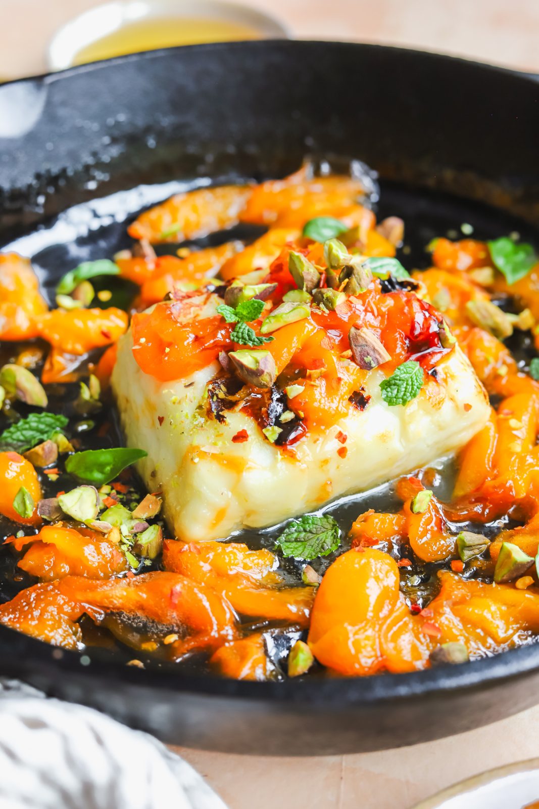 angled photo of grilled halloumi with apricot slices in a cast-iron pan
