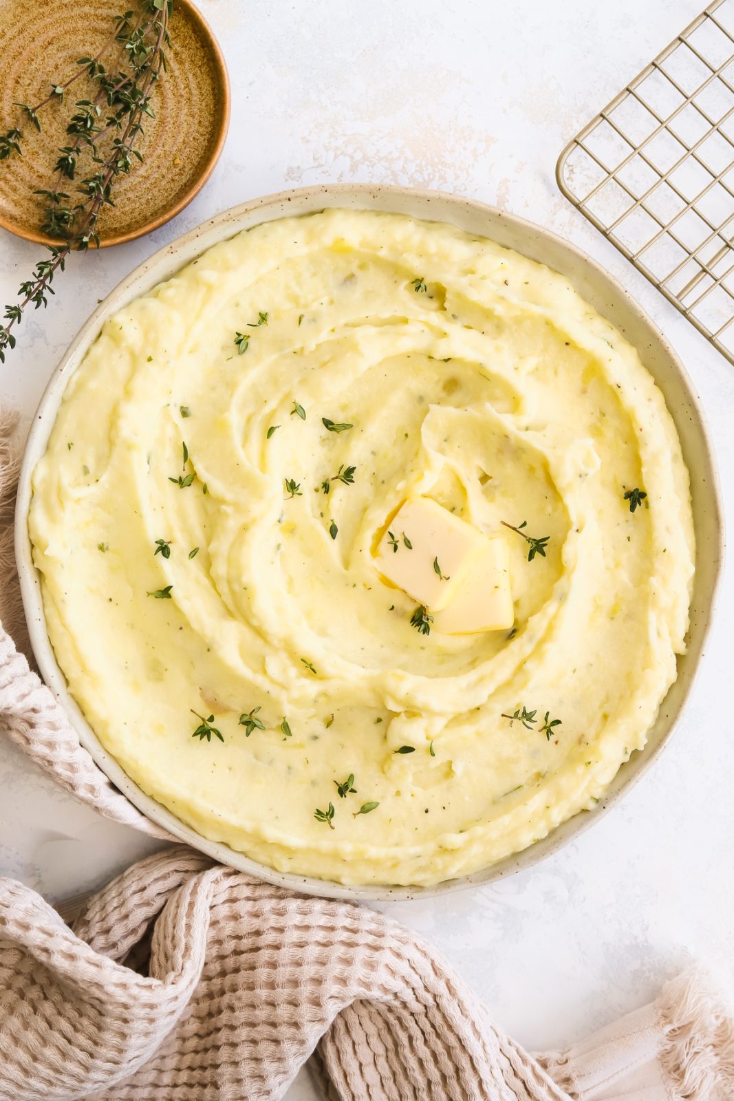 Boursin mashed potatoes in a bowl garnished with thyme leaves and a pat of butter