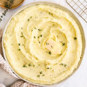 Boursin mashed potatoes in a bowl garnished with thyme leaves and a pat of butter