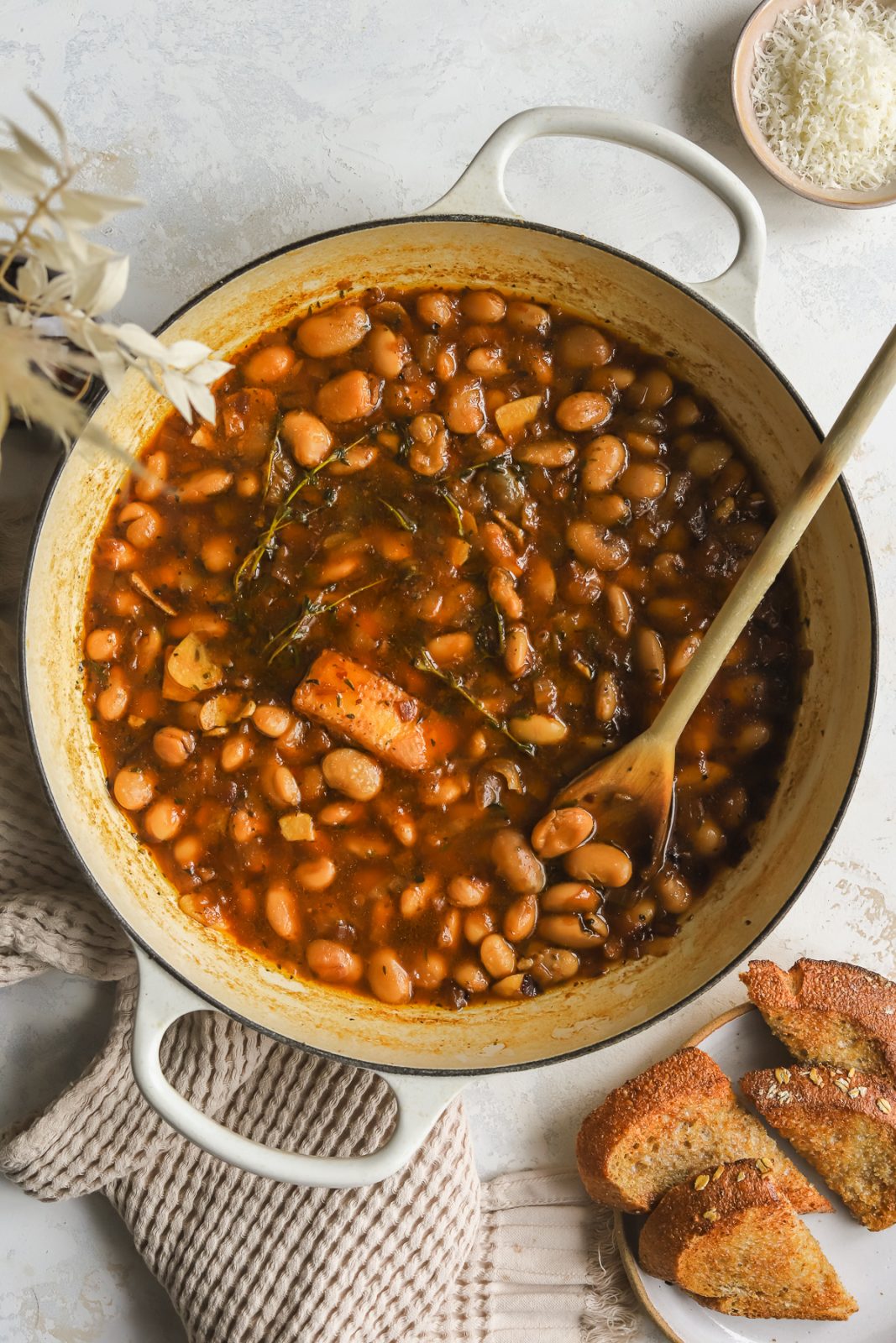 pot with braised white beans, sprigs of fresh thyme and a parmesan rind