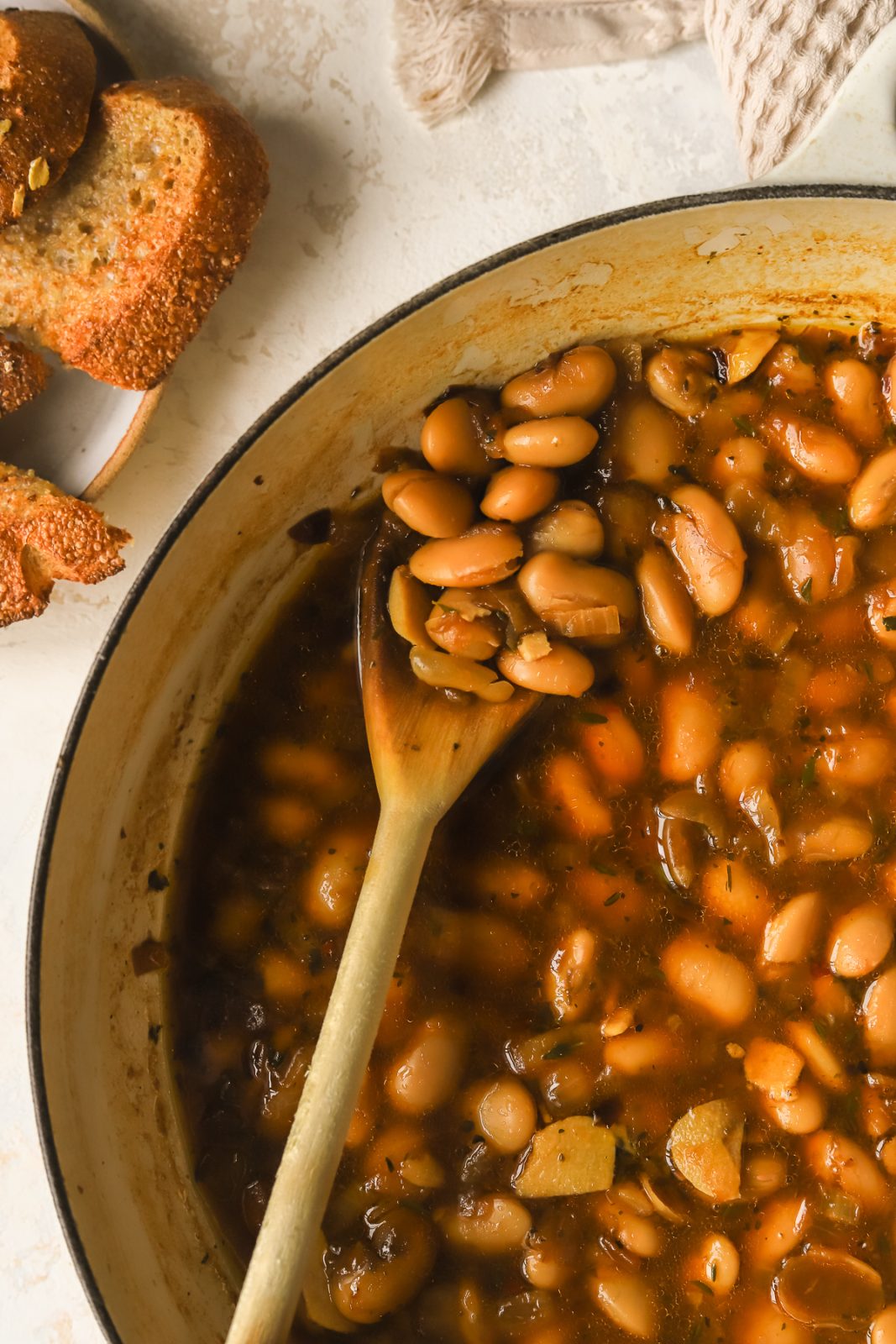 close-up of braised white bean on a wooden spoon in a braiser