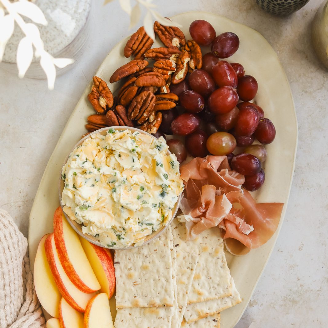 cheese board with cream cheese spread, crackers, apples, pecans, grapes