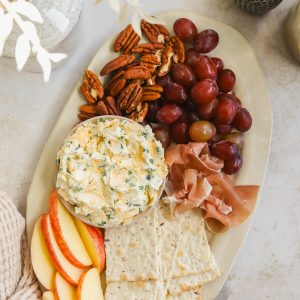 cheese board with cream cheese spread, crackers, apples, pecans, grapes