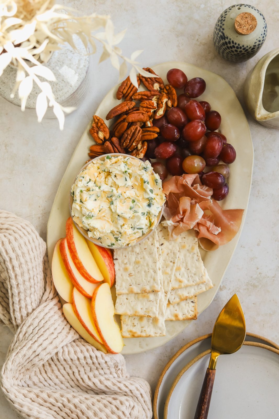 cheese board with cream cheese spread, crackers, apples, pecans, grapes