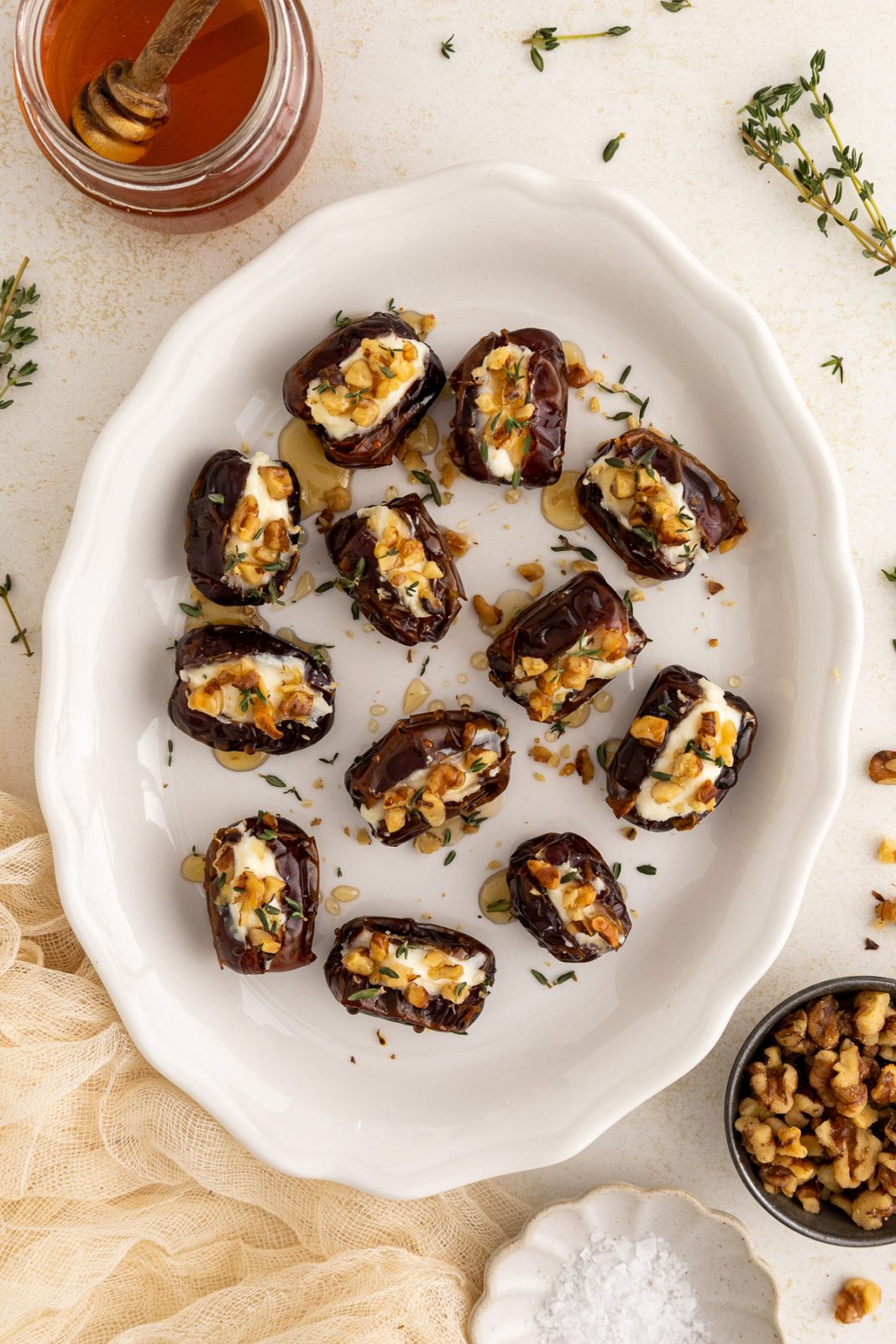 overhead photo of dates in a baking dish stuffed with cream cheese, topped with chopped walnuts, drizzled with honey and garnished with fresh thyme leaves