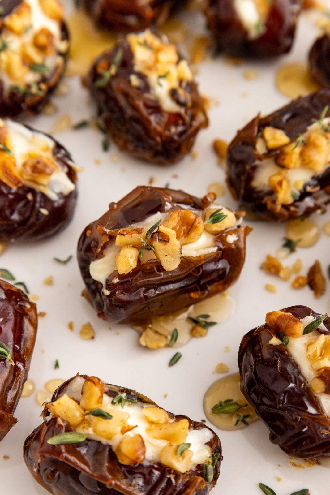 close up of dates stuffed with cream cheese, topped with chopped walnuts, drizzled with honey and garnished with fresh thyme leaves