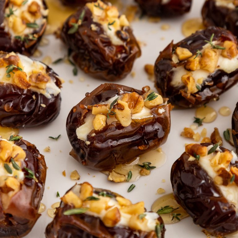 close up of dates stuffed with cream cheese, topped with chopped walnuts, drizzled with honey and garnished with fresh thyme leaves