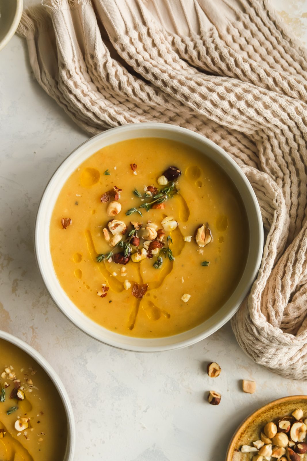 creamy parsnip soup in a bowl garnished with olive oil drizzle, chopped hazelnuts and fresh thyme