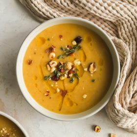 creamy parsnip soup in a bowl garnished with olive oil drizzle, chopped hazelnuts and fresh thyme