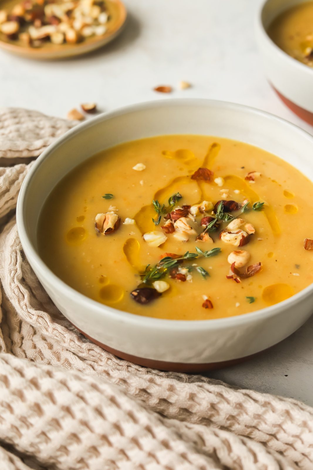 angled photo of a bowl of creamy parsnip soup garnished with olive oil drizzle, chopped hazelnuts and fresh thyme