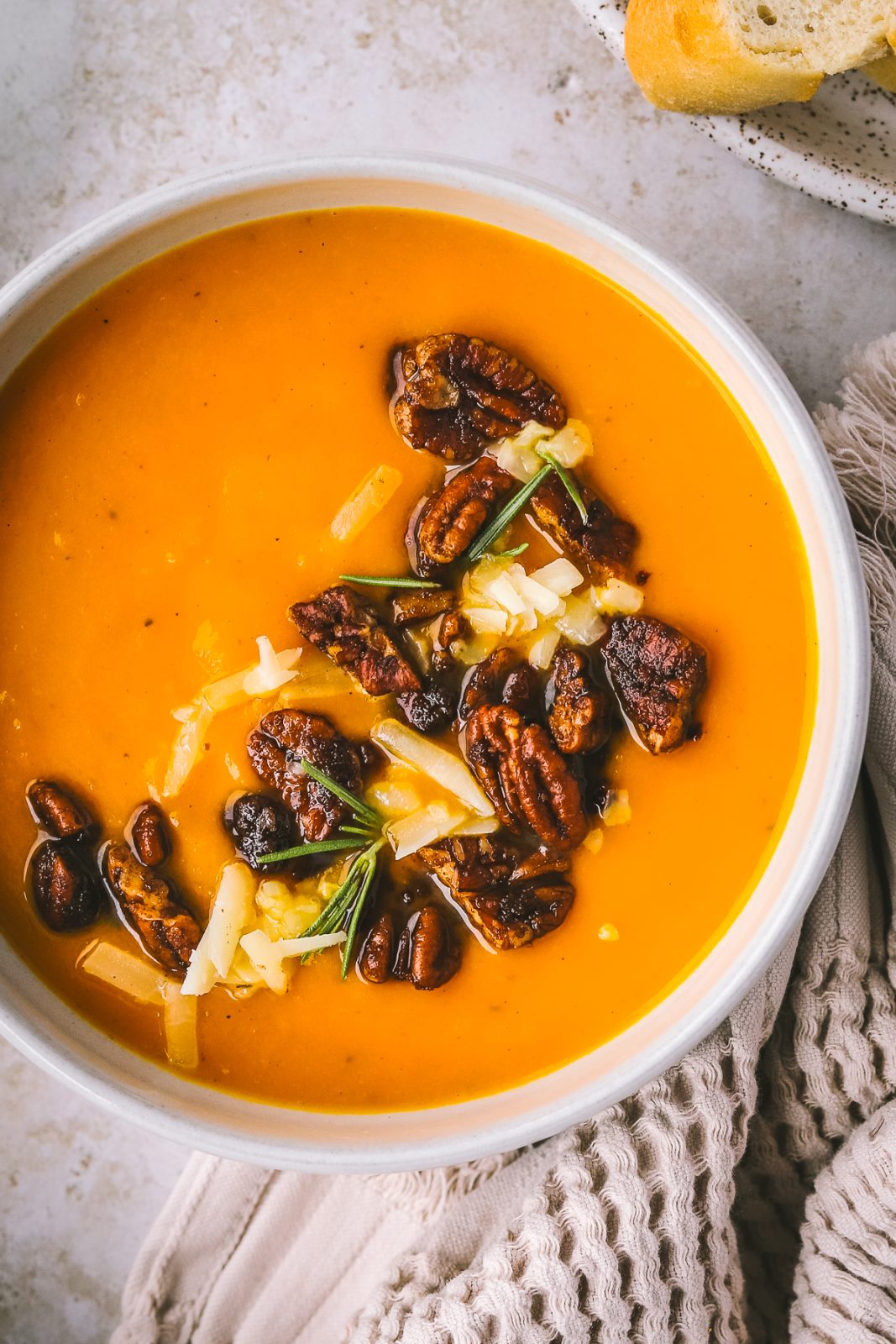 close-up of bowl of sweet potato carrot soup topped with buttery pecans and sharp cheddar cheese