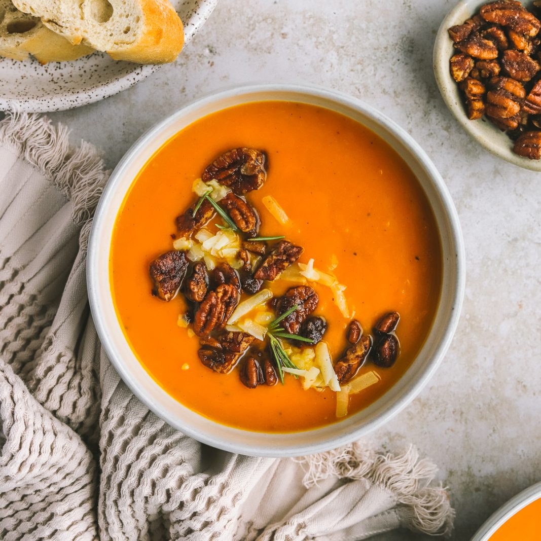 a bowl of sweet potato soup topped with buttery pecans and sharp cheddar cheese